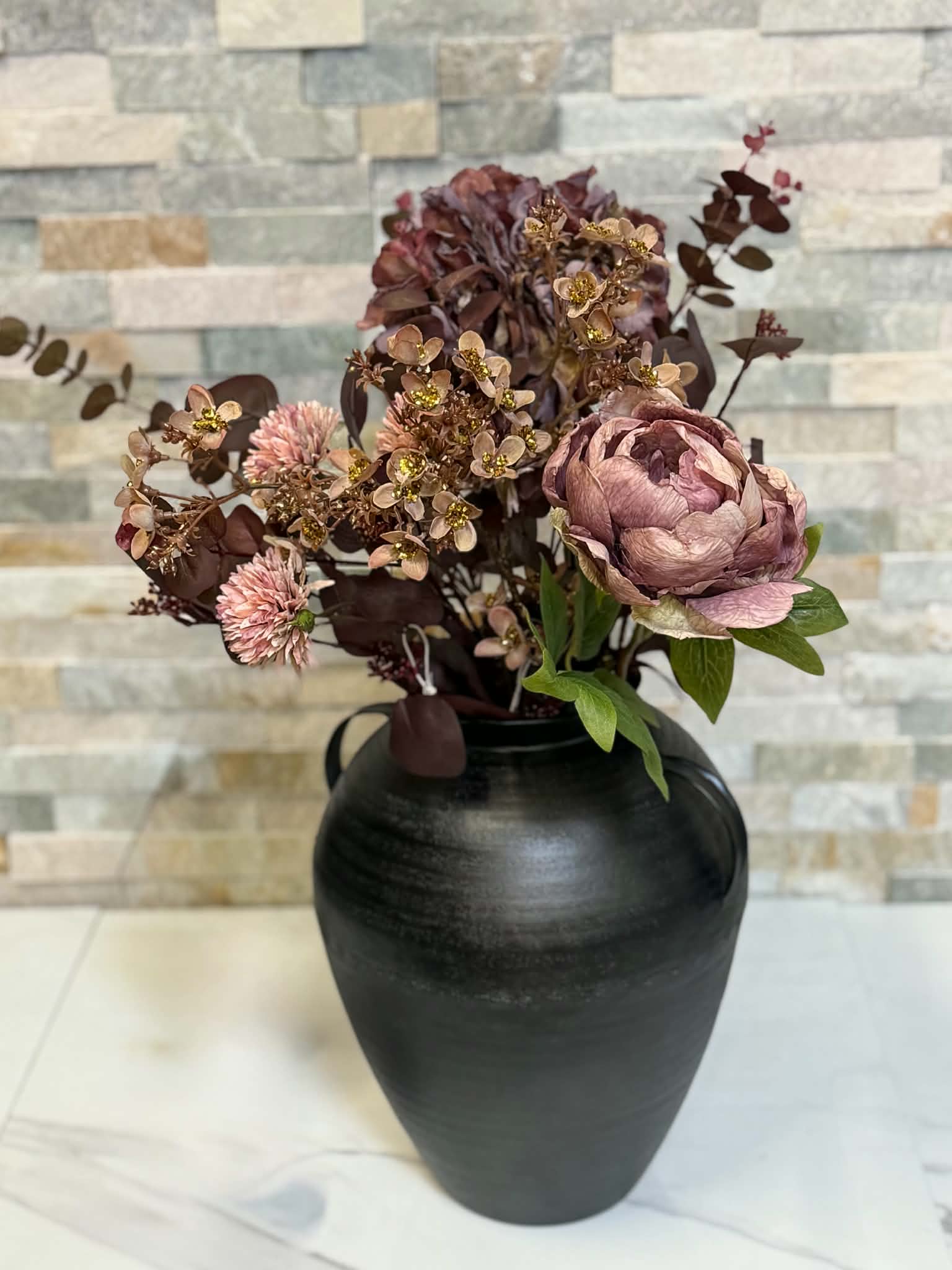 Blomsterarrangemang i rosa och vinröda toner i svart vas