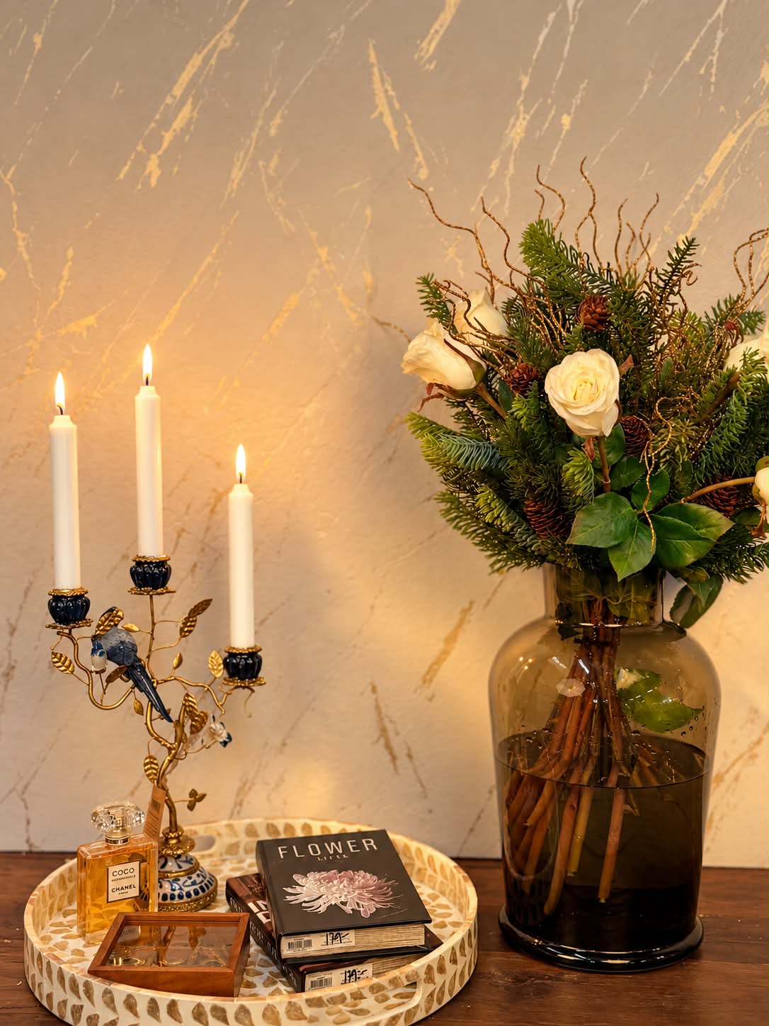 Juldekoration med blommor och gröna kvistar i brun glasvas, tillsammans med tända ljus och dekorativa detaljer.