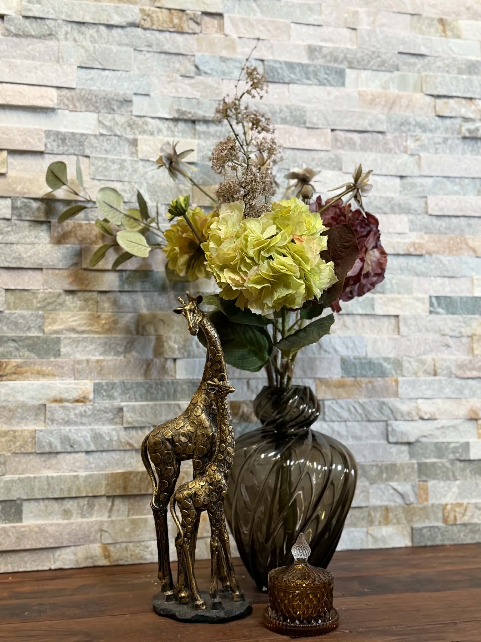 Blomsterarrangemang med gula, rosa och mörkröda blommor i en mörk vas.