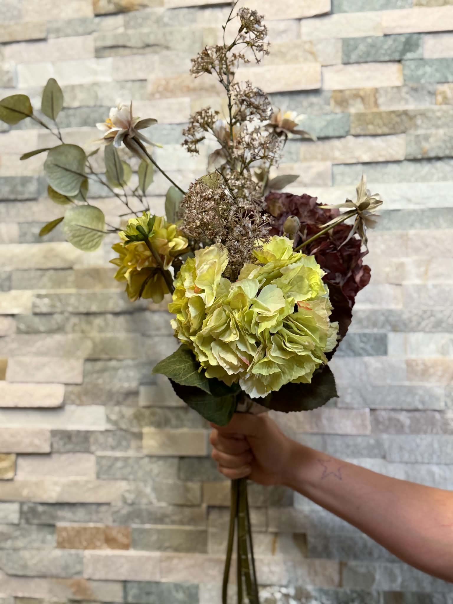 Blomsterbukett med gula, rosa och mörkröda blommor i en mörk vas.