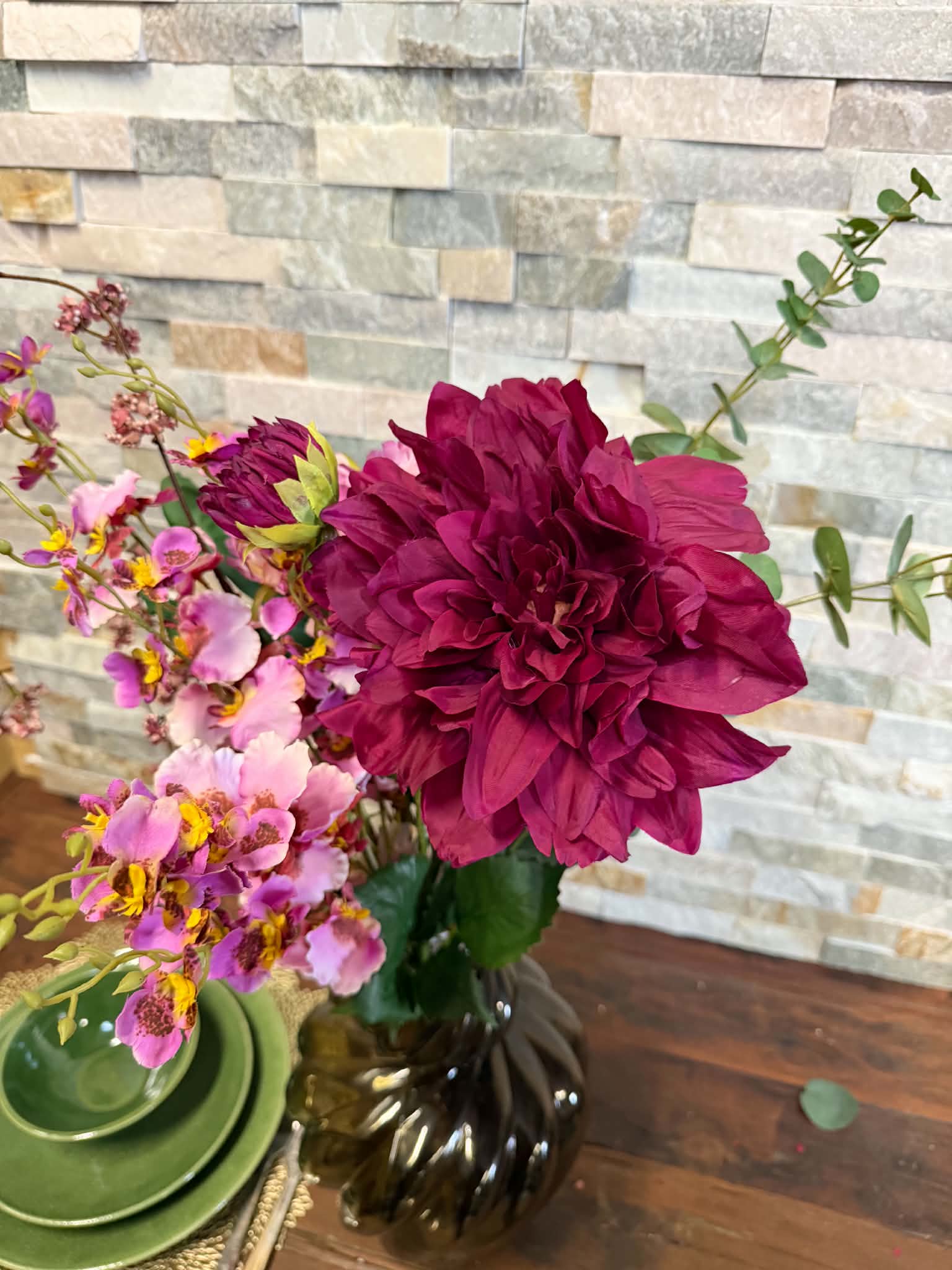 En färgstark blomsterbukett med en stor mörkröd blomma, rosa småblommor och gröna blad i en mörk vas.