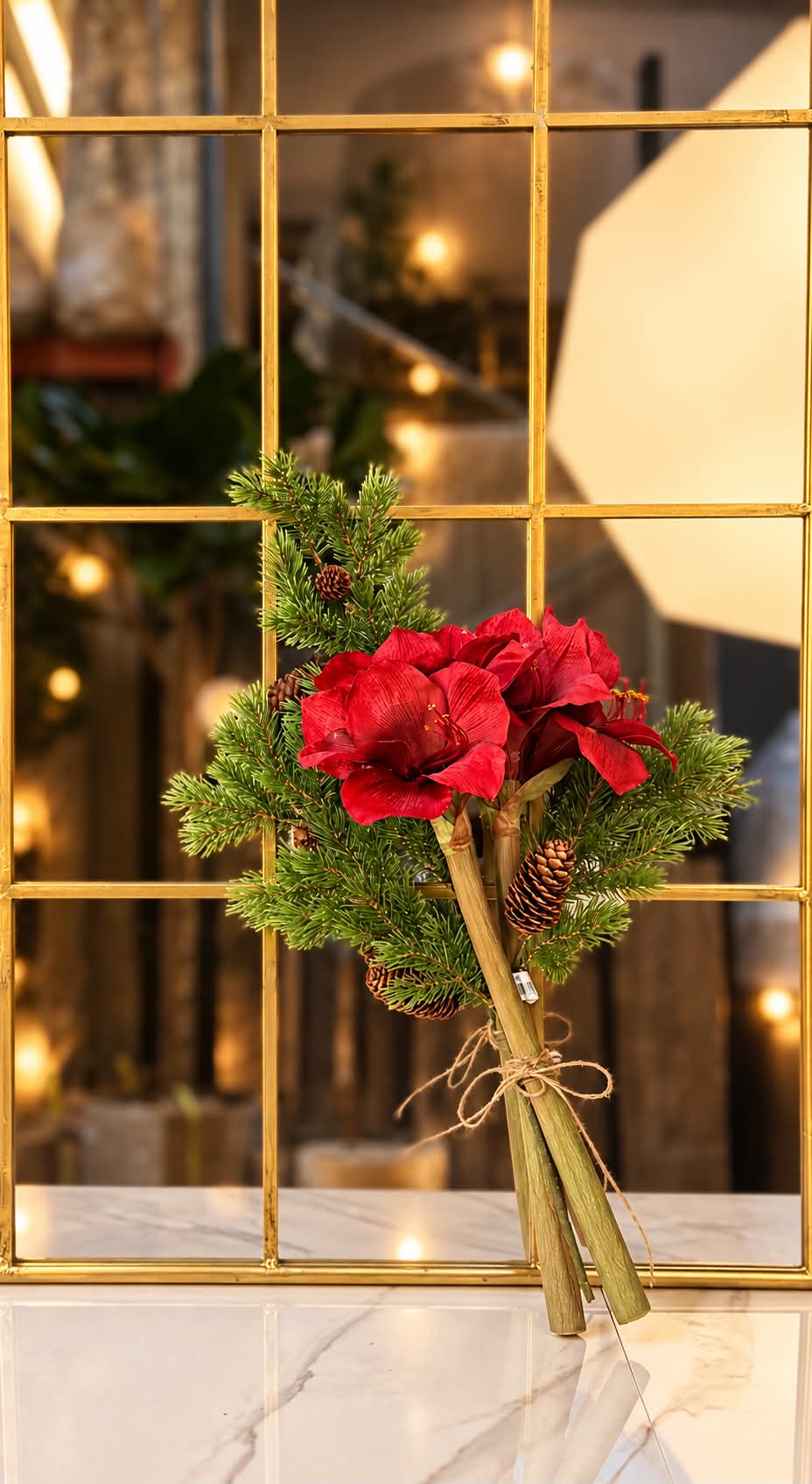 Konstgjord amaryllisbukett 50 cm med röda blommor och granris i vas framför ett julpyntat fönster
