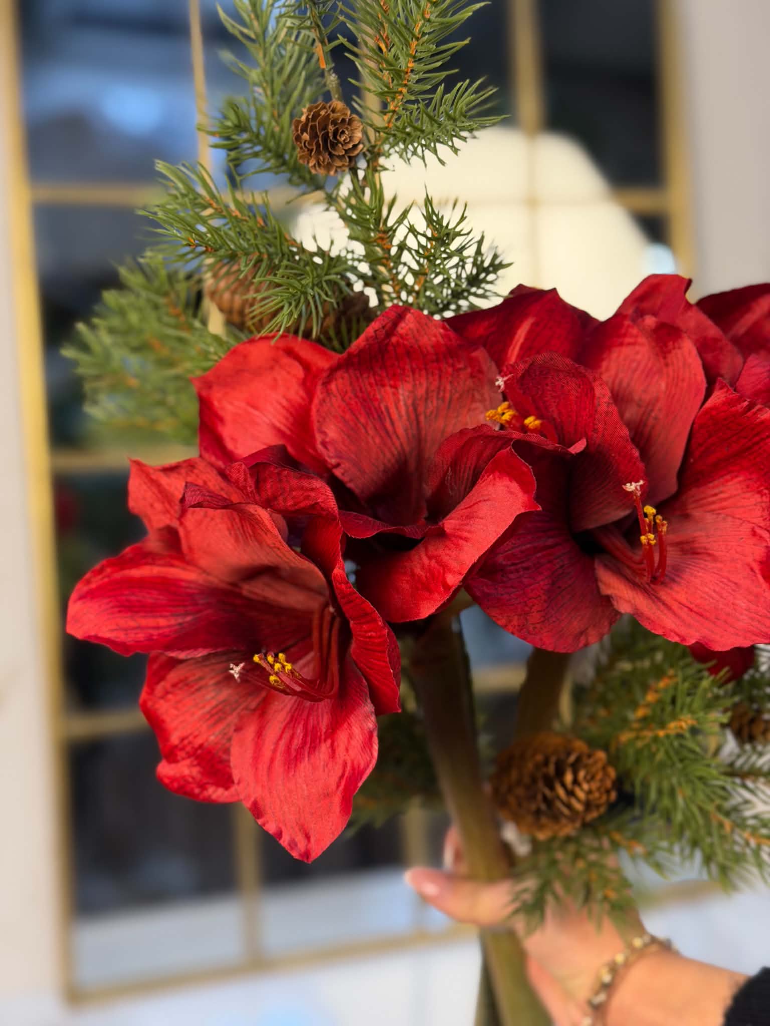Röda konstgjorda amaryllisblommor med grönt granris och kottar i en juldekorerad miljö